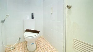 A small, clean bathroom with white tiles, a toilet, a towel, and a shower hose. - Relaxing Studio Room At Suites @Metro Apartment (Bandung)