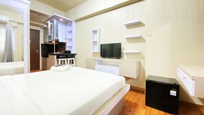 A modern hotel room with a large bed, a TV, a small kitchen area, and a desk. - Relaxing Studio Room At Suites @Metro Apartment (Bandung)