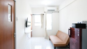 A small, bright room with a sofa, a flat-screen TV, a refrigerator, and an air conditioning unit. - Modern And Homey 2Br At Puncak Kertajaya Apartment (Surabaya)