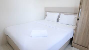 A neatly made bed with white linens and pillows, a wooden wardrobe to the right, and a clean, minimalist room design.