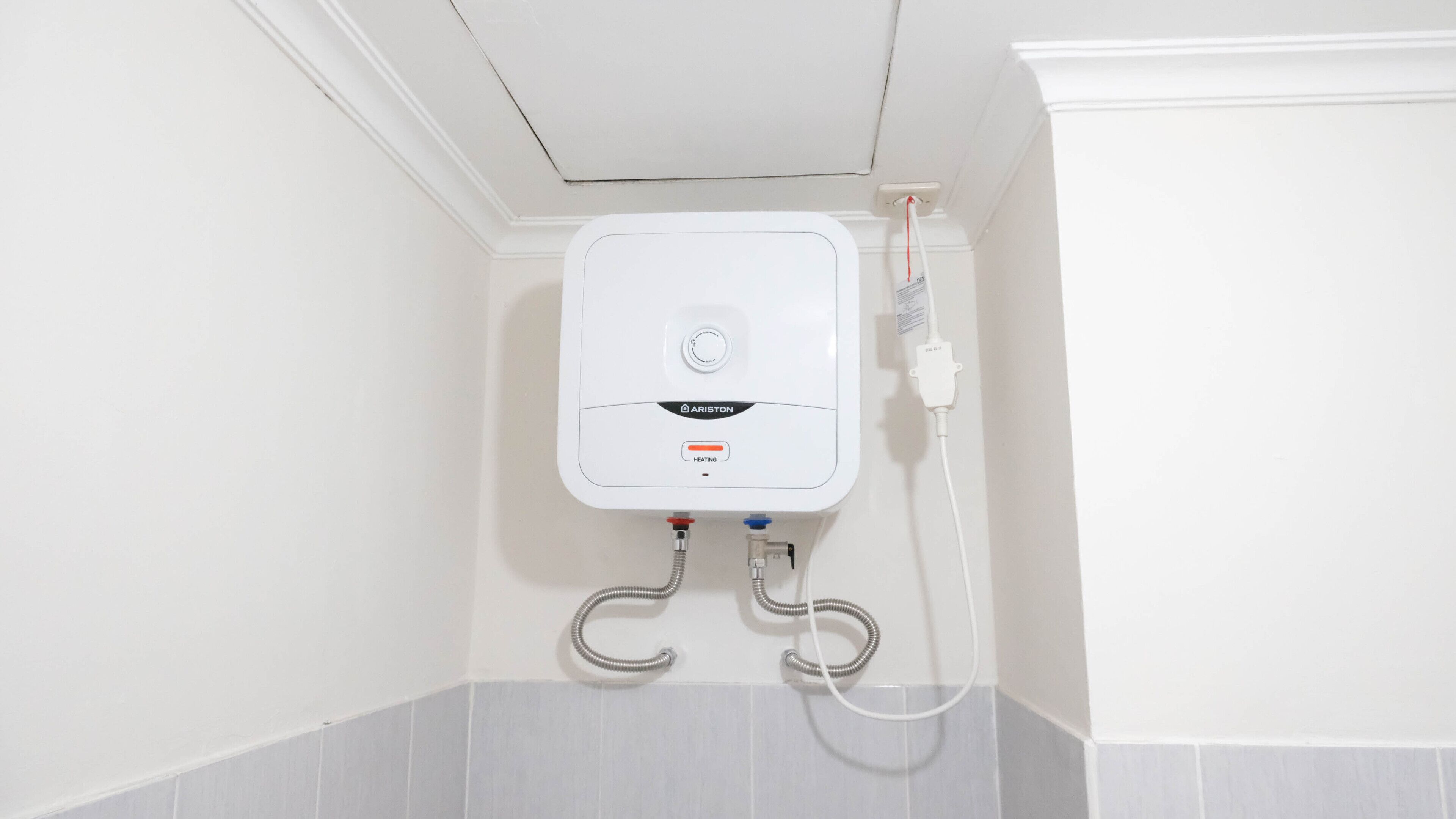 Un chauffe-eau blanc, fixé au mur, doté d’un panneau de commande et de deux tuyaux flexibles.