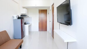 A modern kitchen with a built-in oven, a refrigerator, and a microwave. There is a wooden door leading to another room. A flat-screen TV is mounted on the wall. - Modern And Homey 2Br At Puncak Kertajaya Apartment (Surabaya)
