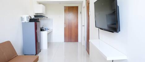 Una cocina moderna con horno empotrado, refrigerador y microondas. Una puerta de madera conduce a otra habitación. Un televisor de pantalla plana está montado en la pared.