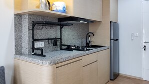 Une cuisine compacte dotée d’un plan de travail en granit, d’une cuisinière encastrée, d’un réfrigérateur en acier inoxydable et d’une étagère suspendue pour les ustensiles.