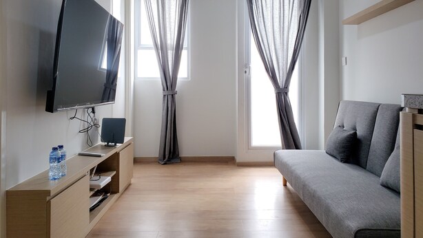 Un salon moderne doté d’un téléviseur à écran plat, d’un meuble de rangement en bois, d’un canapé gris et de deux fenêtres ornées de rideaux gris.