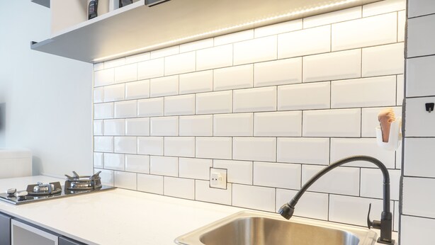 Een keuken met witte metrotegels, een roestvrijstalen spoelbak en een moderne kraan.