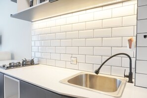 A kitchen with white subway tiles, a stainless steel sink, and a modern faucet. - Cozy Studio At Tifolia Apartment (Jakarta)
