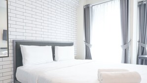 Een net opgemaakt bed met witte lakens, een grijs hoofdeinde en een paar opgerolde handdoeken op het bed.