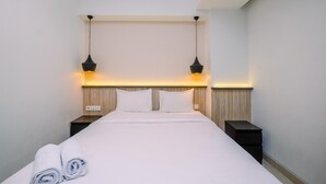 Un lit bien fait, avec du linge de lit blanc et deux oreillers, flanqué de deux tables de chevet sur lesquelles reposent deux lampes noires.
