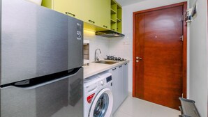 Une cuisine de taille réduite, dotée d’un réfrigérateur en acier inoxydable, d’un lave-linge et d’une porte en bois.