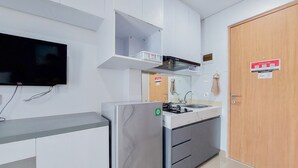 A modern kitchen with a built-in stove, a flat-screen TV, and a wooden door. - Cozy Style And Comfort Studio Room Apartment At B Residence (Pagedangan)