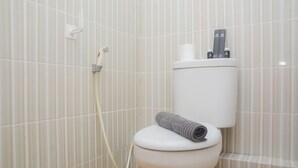 A bathroom with a toilet, a shower, and a toilet paper holder with two bottles. - Comfy And Tidy Studio At Cinere Resort Apartment (Depok)