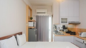 A hotel room with a bed, a small kitchenette, a refrigerator, a microwave, and a window with a curtain. - Comfy And Tidy Studio At Cinere Resort Apartment (Depok)