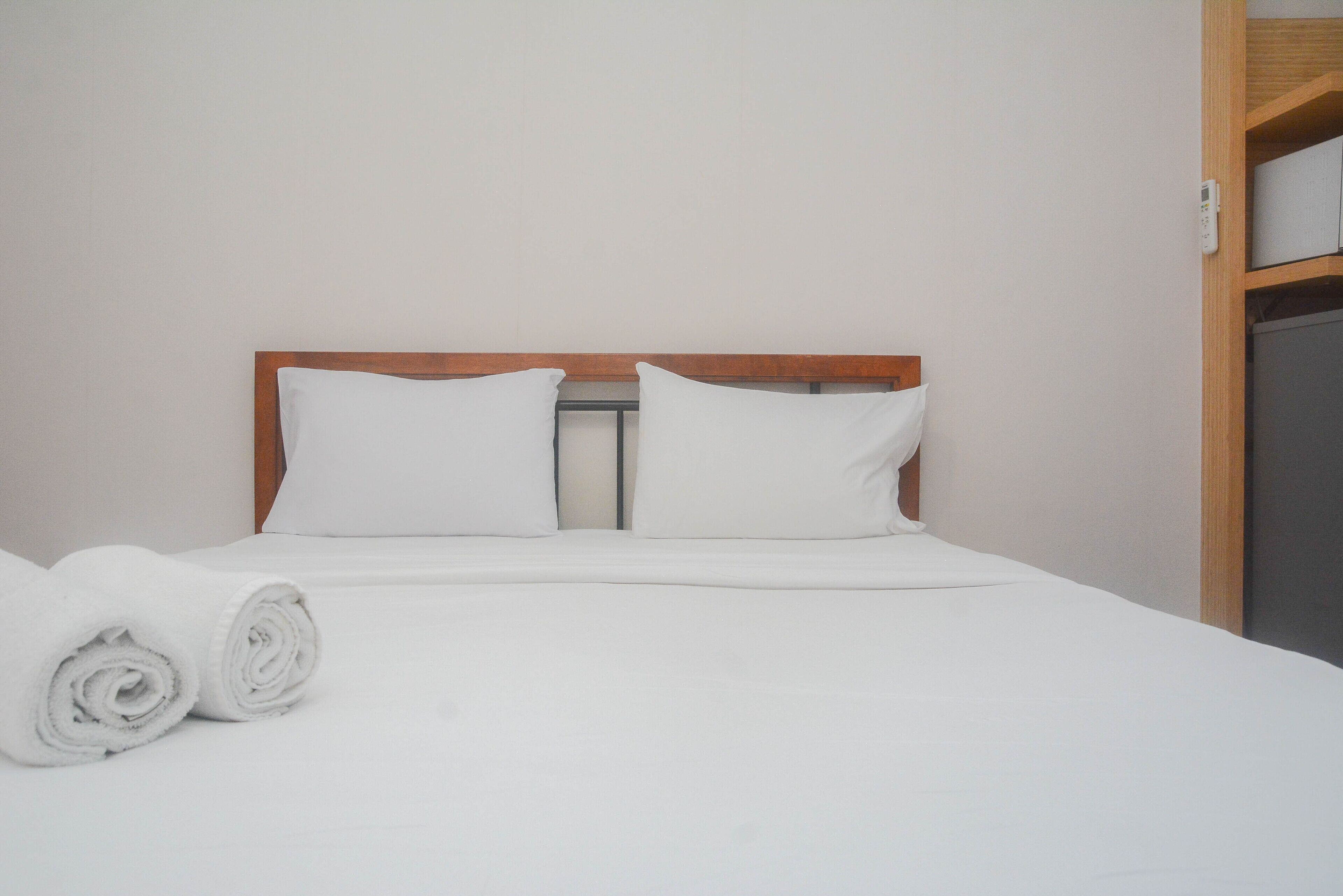A neatly made bed with white linens and pillows, a wooden headboard, and a small wooden shelf unit to the right.