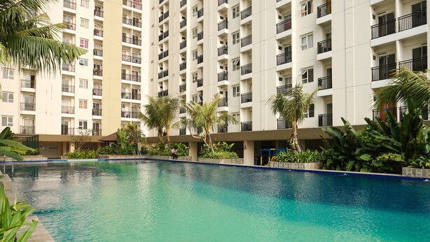 A swimming pool surrounded by a high-rise building with balconies. - Comfy And Tidy Studio At Cinere Resort Apartment (Depok)