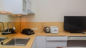 A compact kitchen with a sink, a toaster, a kettle, and a television. - Comfy And Tidy Studio At Cinere Resort Apartment (Depok)