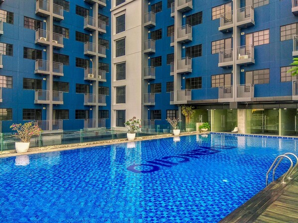 Ein Swimmingpool mit blauem Mosaikfliesenmuster, umgeben von einem modernen Gebäude mit Balkonen und Glasfenstern.