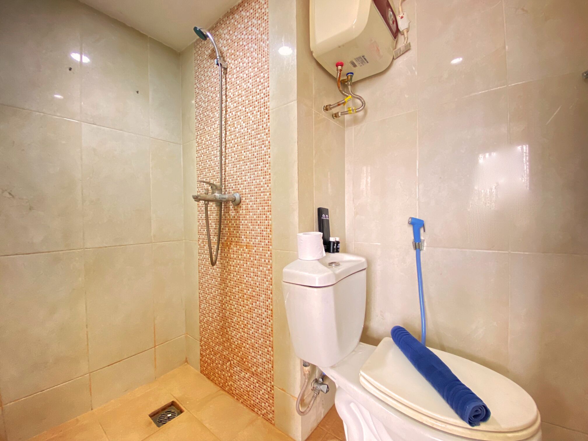 A bathroom with a shower, toilet, and a blue towel on the toilet seat.