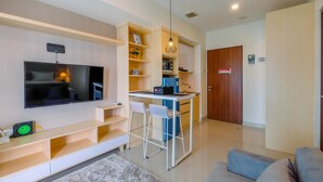 A modern living room with a flat-screen TV, a small kitchen area with a microwave, and a dining space with two chairs. - Cozy And Great Choice Studio At Grand Kamala Lagoon Apartment (Bekasi)