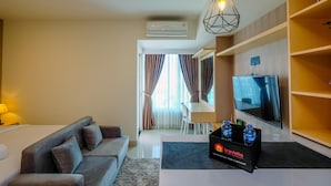 A modern hotel room with a sofa, a dining area, a TV, and a minibar. - Cozy And Great Choice Studio At Grand Kamala Lagoon Apartment (Bekasi)