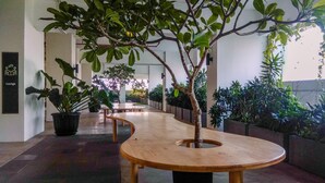 A corridor with potted plants, a wooden bench, and a sign indicating a lounge area. - Cozy And Great Choice Studio At Grand Kamala Lagoon Apartment (Bekasi)