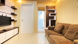 A modern living room with a flat-screen TV, built-in shelves, a sofa, and a door leading to another room. - Cozy Living 1Br Apartment At Parahyangan Residence (Bandung)