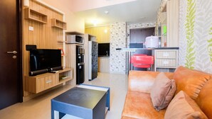 Ein modernes Wohnzimmer mit Flachbildfernseher, Holzregalen, einer Couch und einer Küchenzeile mit Mikrowelle, Kühlschrank und einer kleinen Arbeitsfläche.