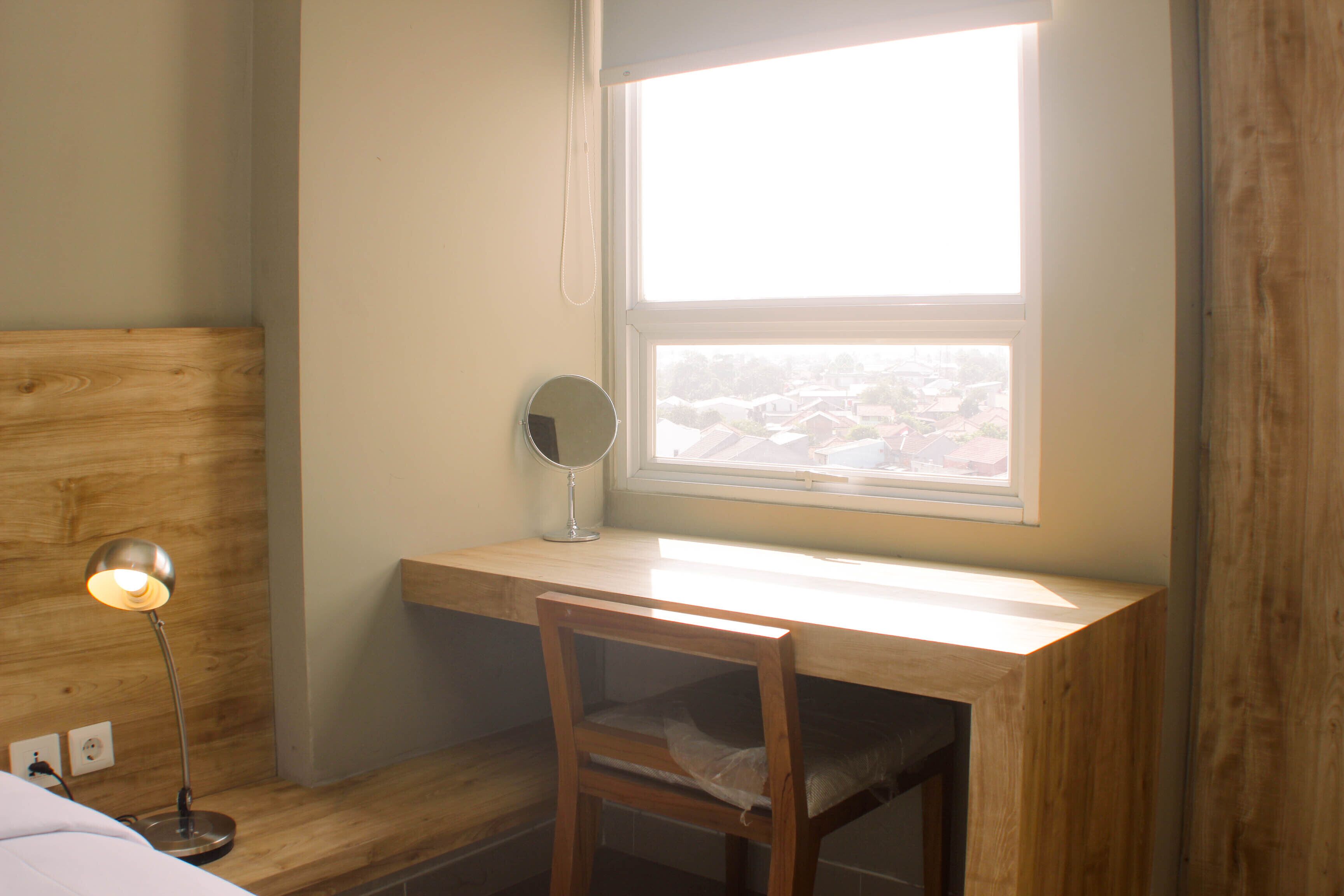 Ein Zimmer mit einem Holztisch, einem Sessel, einer Nachttischlampe und einem Fenster mit Blick auf Gebäude.