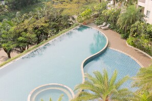 Una grande piscina a forma di curva circondata da vegetazione rigogliosa e un pontile in legno.