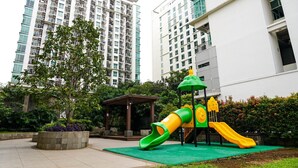 Un parque infantil con toboganes y un árbol verde en un entorno urbano.