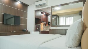 Una habitación de hotel con una cama, un televisor montado en la pared, una zona de cocina con armarios y un microondas, y un espejo grande sobre la cama.