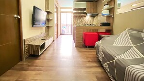 A compact living space with a kitchenette, a TV mounted on the wall, a sofa, and a red ottoman. - Modern And Cozy Stay 2Br Apartment At Gateway Ahmad Yani Cicadas (Bandung)
