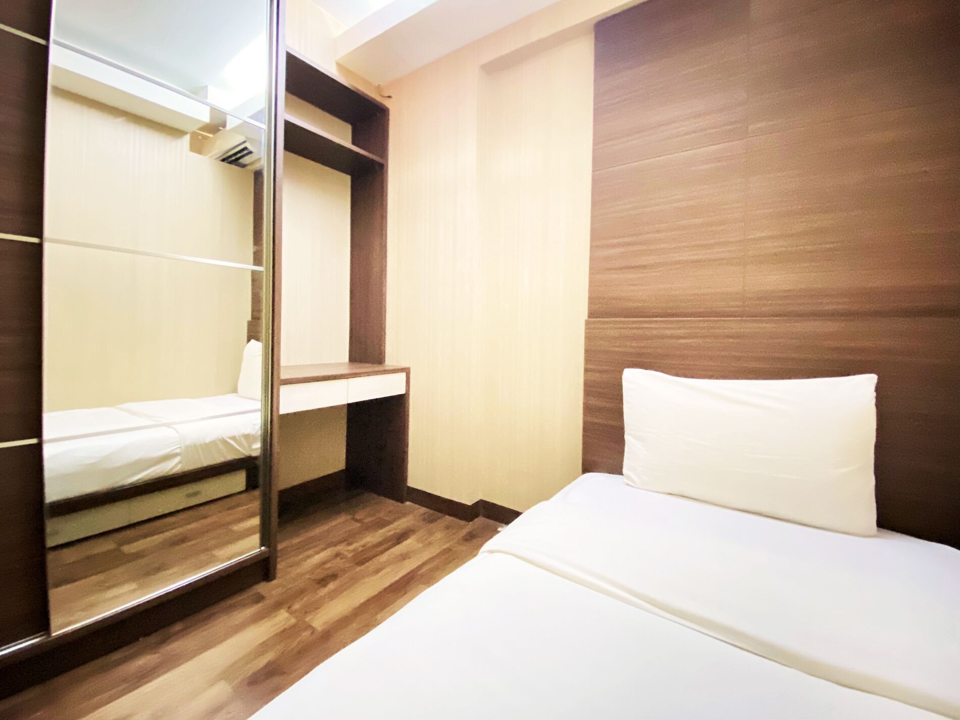 A hotel room with a bed, a mirror, and a wooden wardrobe.