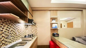 A compact kitchen with a sink, stove, and a small countertop. There are wooden cabinets and a mirror above the countertop. - Modern And Cozy Stay 2Br Apartment At Gateway Ahmad Yani Cicadas (Bandung)