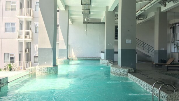 An indoor swimming pool with clear water, surrounded by tiled walls and columns, and a staircase on the right. - Homey Studio Room at Harvard Jatinangor Apartment (Cileunyi)