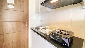 A kitchen with a stove, sink, and wooden door. - Homey Studio Room at Harvard Jatinangor Apartment (Cileunyi)