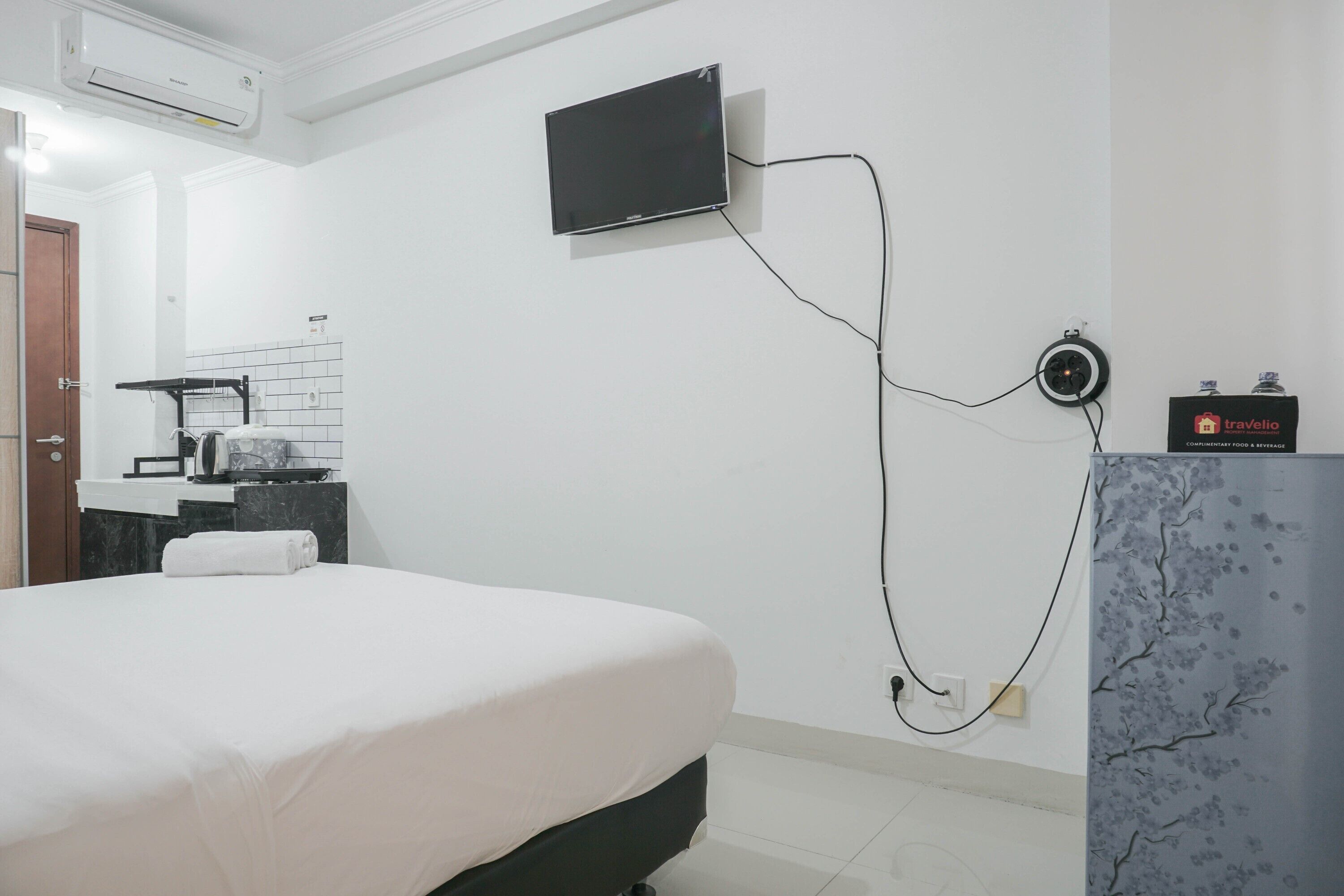 Een hotelkamer met een bed, een aan de muur bevestigde televisie, een minibar en een stopcontact.