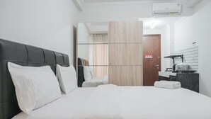 Et hotelværelse med en stor seng, en mørk sengegavl, et spejl, en væg med træpaneler og et badeværelse med et håndvask og et spejl, samt et håndklæde på sengen.