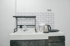 Una cocina moderna con encimera blanca, armarios de mármol negro, un hervidor y una cafetera.