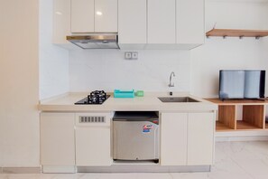 A compact kitchen with a built-in refrigerator, a gas stove, a sink, and a television on a wooden shelf. - Nice And Comfy Studio Apartment At Sky House Bsd (Pagedangan)