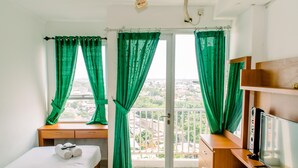 A hotel room with a bed, a desk, a TV, and a balcony with green curtains.