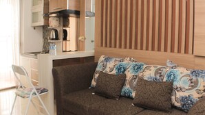 Un espace de vie compact comprenant un coin cuisine, un canapé agrémenté de coussins à motifs floraux et une chaise pliante.