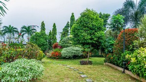 A garden with a stone pathway, various shrubs, and tall trees. - Comfort Stay Studio Room At Margonda Residence 3 Apartment (Depok)