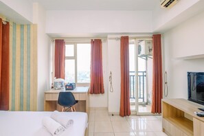 A hotel room with a bed, a desk with a chair, a television, and a balcony with curtains. - Comfort Stay Studio Room At Margonda Residence 3 Apartment (Depok)