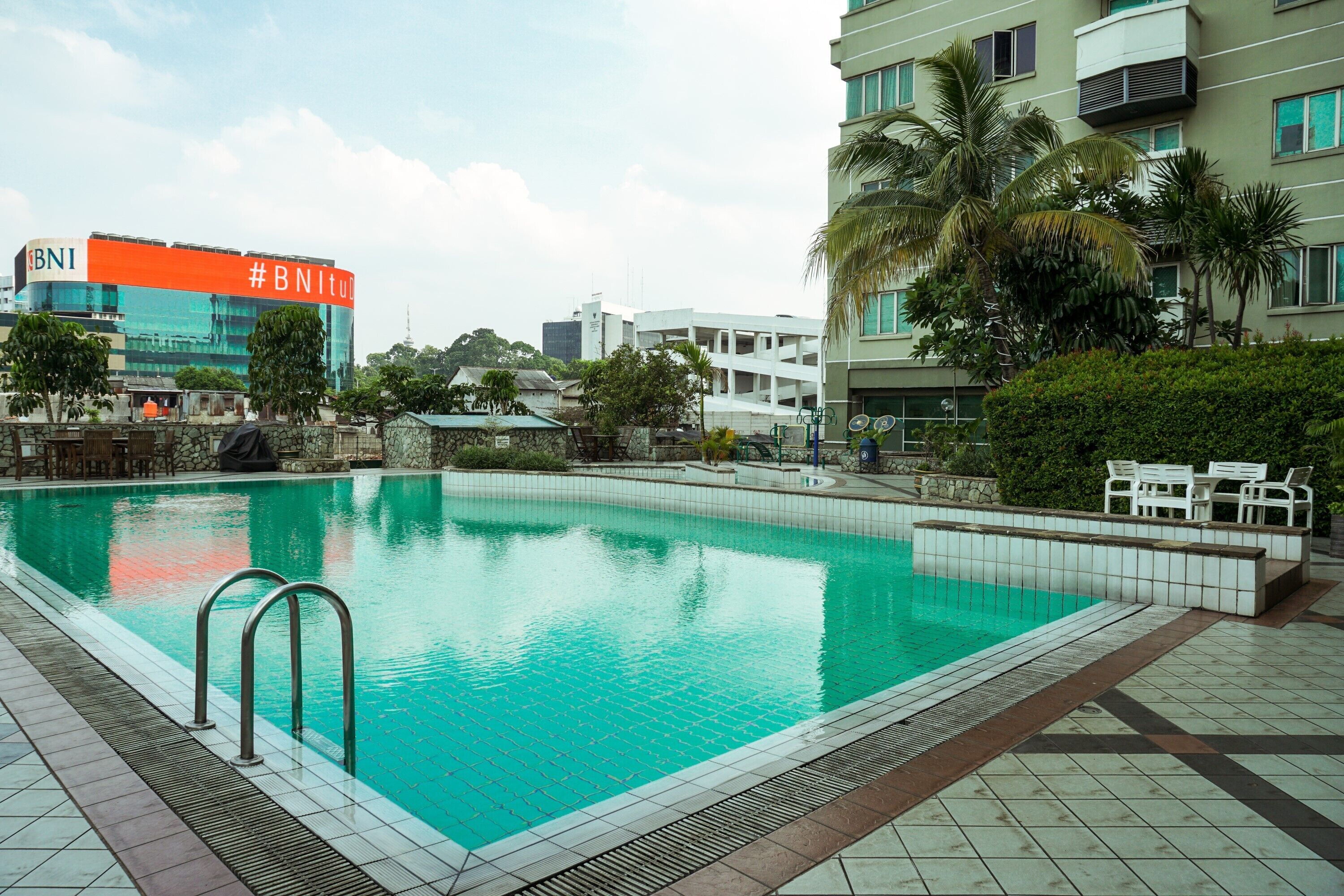 A swimming pool with a tiled deck, surrounded by greenery and a building with a sign reading "BNI".