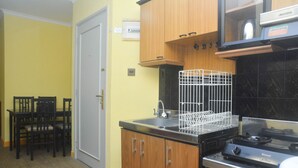 Une cuisine de taille réduite, dotée de meubles en bois, d’un évier et d’une cuisinière. On y trouve également un coin repas avec des chaises et une table.