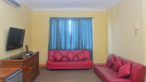 Un salon avec un canapé rouge, un téléviseur posé sur un meuble en bois et un rideau bleu.