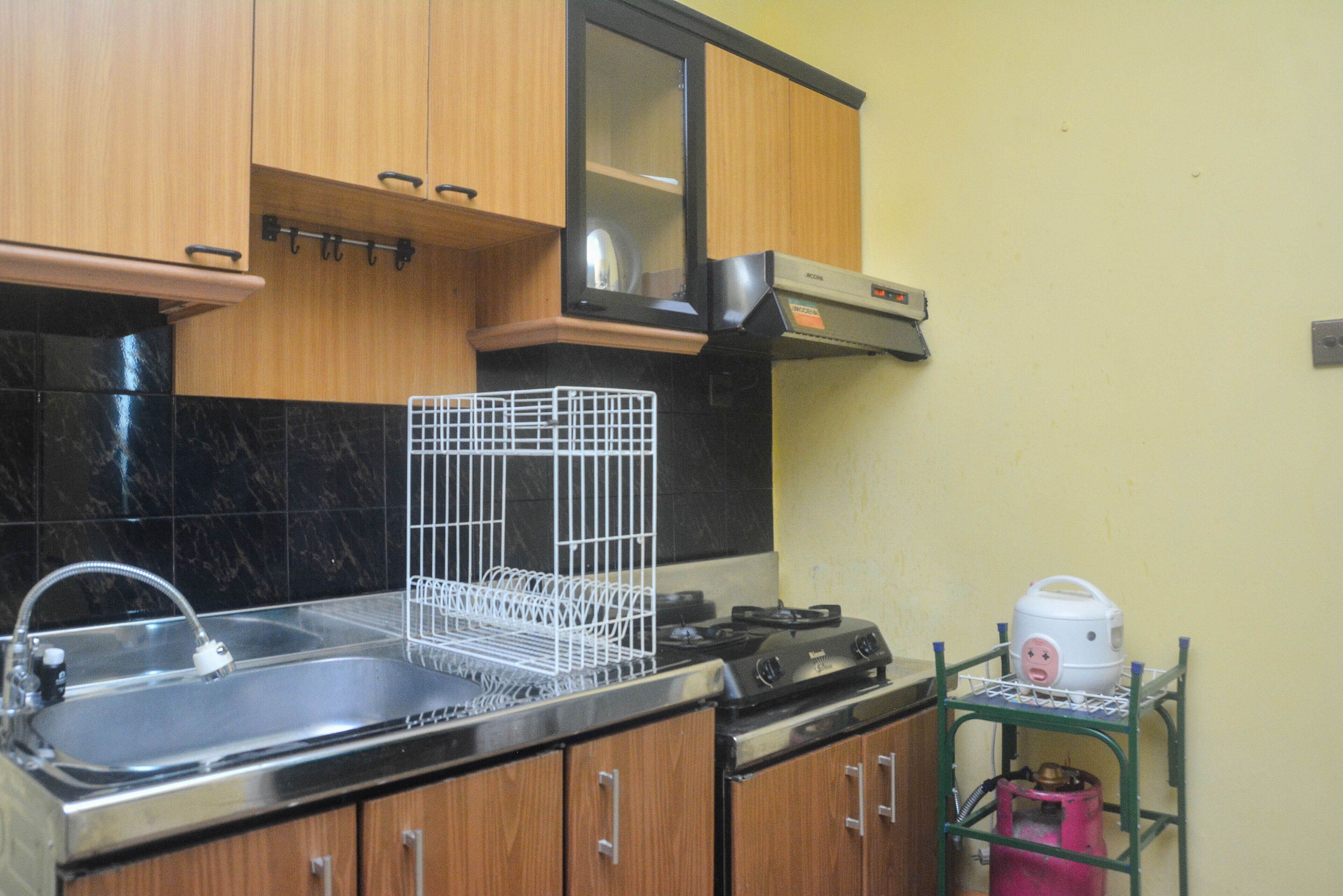 A kitchen with wooden cabinets, a stainless steel sink, a gas stove, and a small cart with a pink container.
