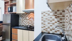 A kitchen with wooden cabinets, a black refrigerator, a stove, and a sink. - Graceful And Cozy 2Br At Signature Park Grande Apartment (Jakarta)