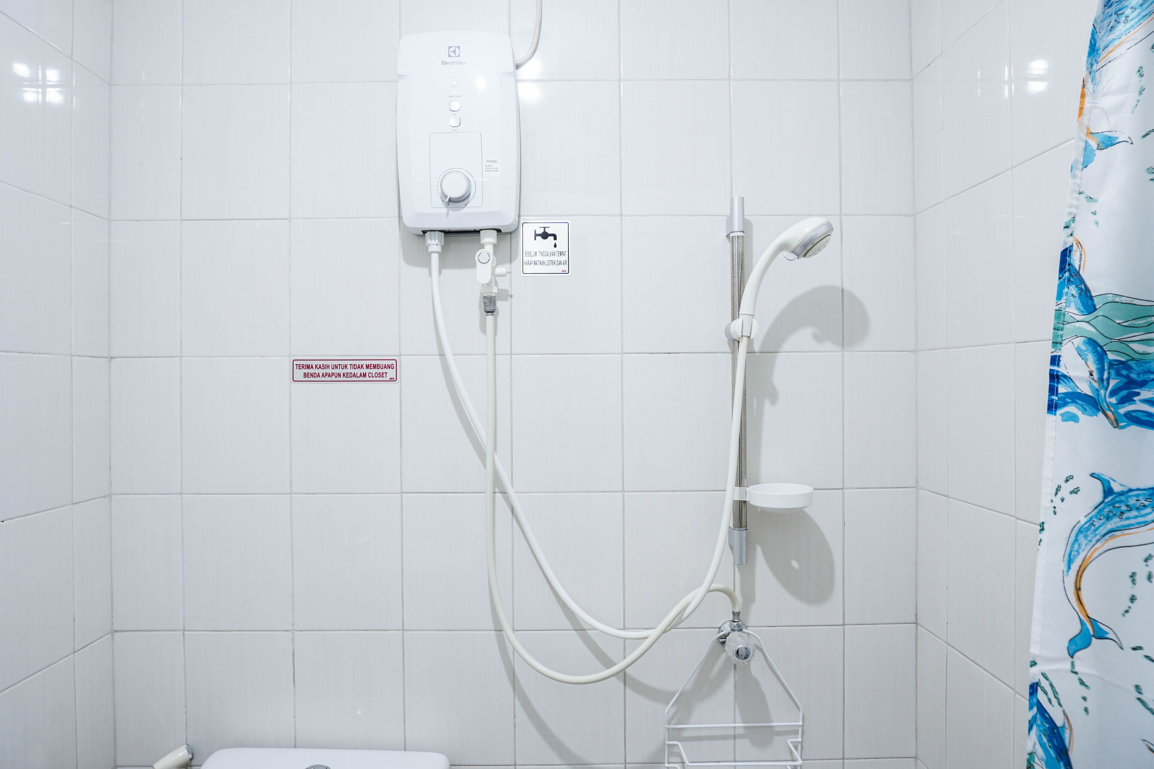 A bathroom with white tiled walls, a shower with a handheld showerhead, and a toilet. There is a sign indicating the shower is for non-smoking use.